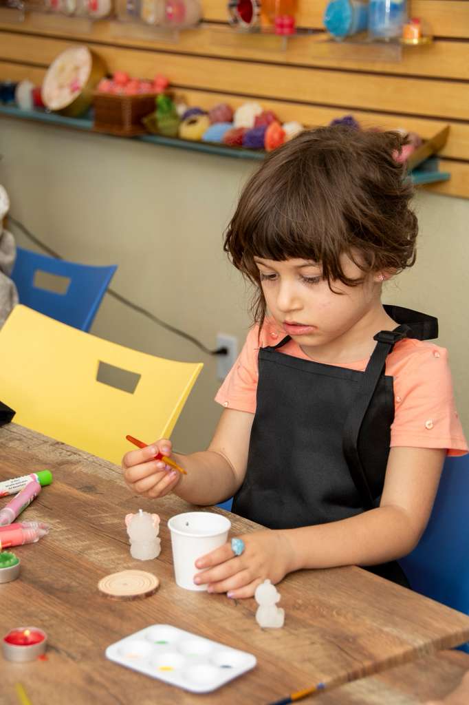 A girl in an apron painting a small bear candle