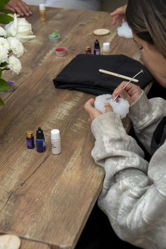 Hands shaping wax beside a row of fragrance oils